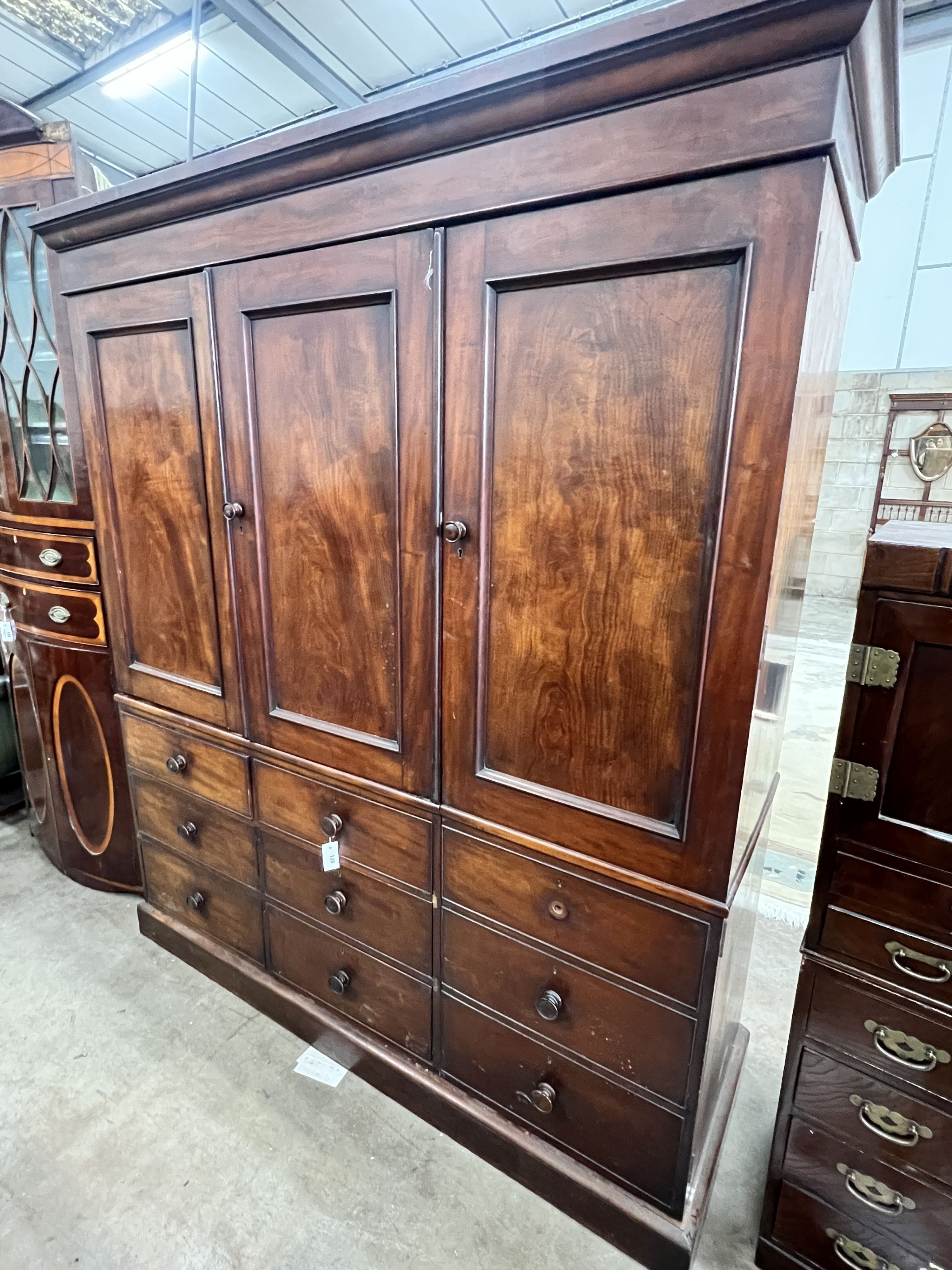 An early Victorian mahogany triple press cupboard, with three panelled doors over an arrangement of drawers and dummy drawers., width 178cm, depth 58cm, height 209cm